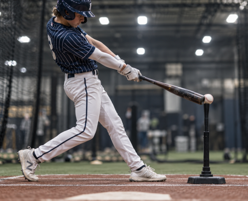 Youth baseball hitter front leg fully braced at impact — demonstrating the blocking position in batting cage
