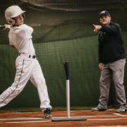 Youth baseball player at the tee with coach — baseball hitting lessons for swing mechanics
