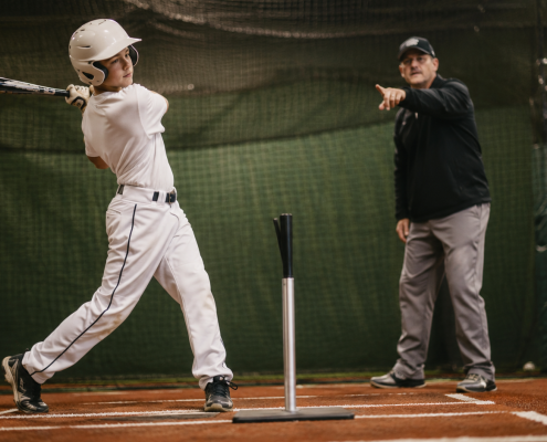Youth baseball player at the tee with coach — baseball hitting lessons for swing mechanics
